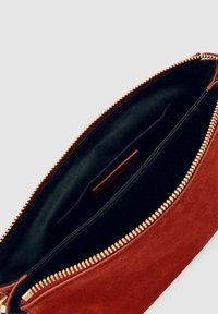 Rdeča nubuk torbica z zlatim zadrgo. Notranjost je podložena s črno tkanino, ima majhen žep in gladko teksturo.