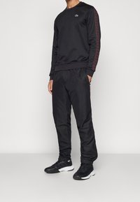 Svart atletisk sweatshirt och byxor med en logotyp på bröstet, med röda sidokanter och elastiska ärmslut och midjeband.