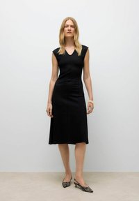 Robe noire, longueur genou avec des manches courtes et un col en V. Tissu lisse avec un corsage ajusté qui s'évasent à la taille.