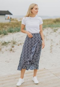 Marineblumige Midikleid mit Rüschensaum, kombiniert mit einem schlichten weißen T-Shirt und weißen Sneakern. Weicher Stoff mit tailliertem Bund.