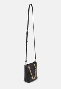 Sort crossbody-taske i imiteret læder med krokodilletekstur og guldkæde, med en lang justerbar rem og rektangulært design.