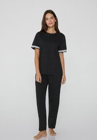 Černý pyžamový set se krátkým rukávem, pokrytý bílými puntíky a krajkovým lemováním, doplněný o odpovídající kalhoty. Měkký materiál, volný střih.