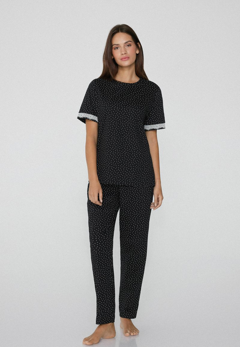 Černý pyžamový set se krátkým rukávem, pokrytý bílými puntíky a krajkovým lemováním, doplněný o odpovídající kalhoty. Měkký materiál, volný střih.
