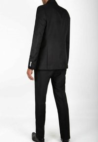 Veste de costume noire ajustée avec une fente simple, assortie à un pantalon. La veste présente quatre boutons blancs aux poignets et un design élégant.