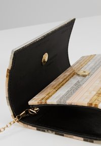 Clutchväska med svart inredning, tryckknappslås, guldkedja och utsidan dekorerad med glänsande beige, guld, silver och vita mosaikplattor.