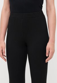 Pantalons de yoga noirs en stretch avec une texture lisse, dotés d'une taille haute et d'une coupe ajustée. Pas de matériel ou de motifs visibles.