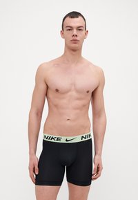 Črne športne kratke hlače z mehkimi rjavimi Nike logotipom na pasu, prilegajočega se dizajna in gladke teksture. Primerne za športno uporabo.