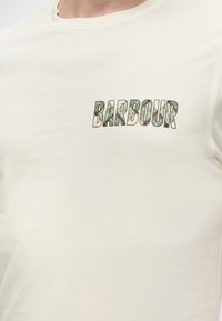 Κρεμ T-shirt με το κείμενο "BARBOUR" σε πολύχρωμο σχέδιο καμουφλάζ στο αριστερό στήθος.