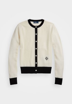 Cardigan blanc avec bordure noire sur le col, la ligne de boutons, les poignets et l'ourlet, comportant sept boutons blancs et un petit logo noir en bas devant.