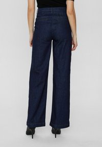 Wide-leg denim jeans in dark blue, featuring a high waist, clean design, and contrasting stitching. Hem hits above shoes with a slight flare.