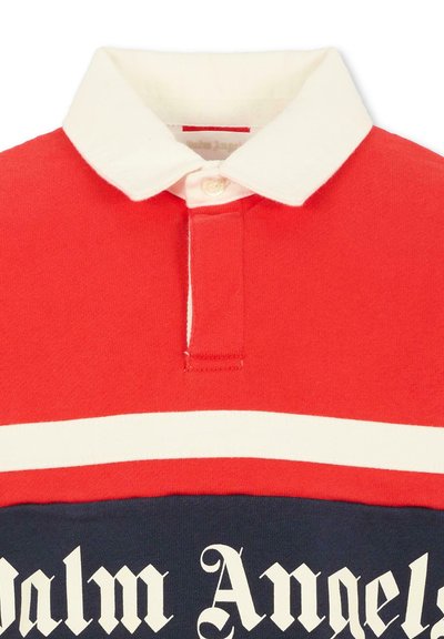 Rode en marineblauwe rugbyshirt met witte kraag, een witte horizontale streep en tekst in gotische stijl die gedeeltelijk "Palm Angels" leest.