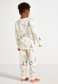 Kremowy zestaw piżamowy z zabawnymi niebieskimi ilustracjami chmur, drzew i zwierząt. Miękka tkanina z długimi rękawami i mankietami.