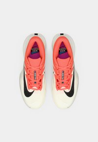 Αθλητικά παπούτσια τένις Nike με κοραλλί επάνω μέρος, λευκή υφή στη μέση σόλας, μαύρο σήμα Swoosh και μοβ εσωτερικό, με επίπεδα κορδόνια και ενισχυμένη περιοχή στη μύτη.