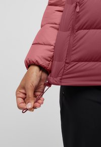 Veste puffer rose avec un design matelassé, dotée d'un ajustement à cordon au niveau de l'ourlet. Le tissu semble lisse et résistant à l'eau.