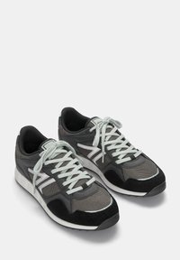 Graue Sport Schuhe aus Mesh und Wildleder mit weißen Akzenten, flachen Schnürsenkeln und einer schwarzen Gummisohle. Runde Zehenpartie und gepolsterter Schaft.