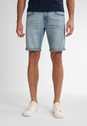 Shorts en denim bleu clair avec ourlets roulés, dotés de cinq poches et d'une coupe droite, portés avec des baskets blanches.
