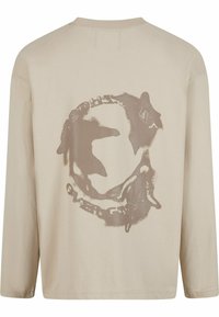 Beige Baumwoll-T-Shirt mit langen Ärmeln, das auf der Rückseite ein verblasstes braunes Motiv von Walen und Text zeigt. Mit Rundhalsausschnitt und lockerem Schnitt.