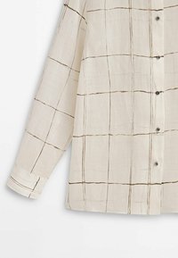Langærmet skjorte i lys beige stof med brunt rutemønster, med knapper foran og ved mansjetterne. Glat tekstur.