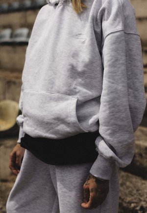 Gray hoodie with a front pocket and black waistband, features ribbed cuffs, soft texture, and relaxed fit. Accompanied by matching gray pants.