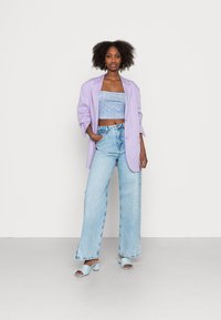 Blazer oversized lavanda sobre um crop top azul claro, combinado com jeans de perna larga de denim claro de cintura alta e sandálias de bloco azul.
