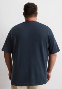 Donkerblauwe katoenen T-shirt met korte mouwen, een ronde hals en een rechthoekig label op de bovenrug. Glad oppervlak en losse pasvorm.