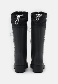 Black waterproof rubber boots with a textured fur cuff, adjustable drawstring, and branding along the side. Rectangular design and flat sole.