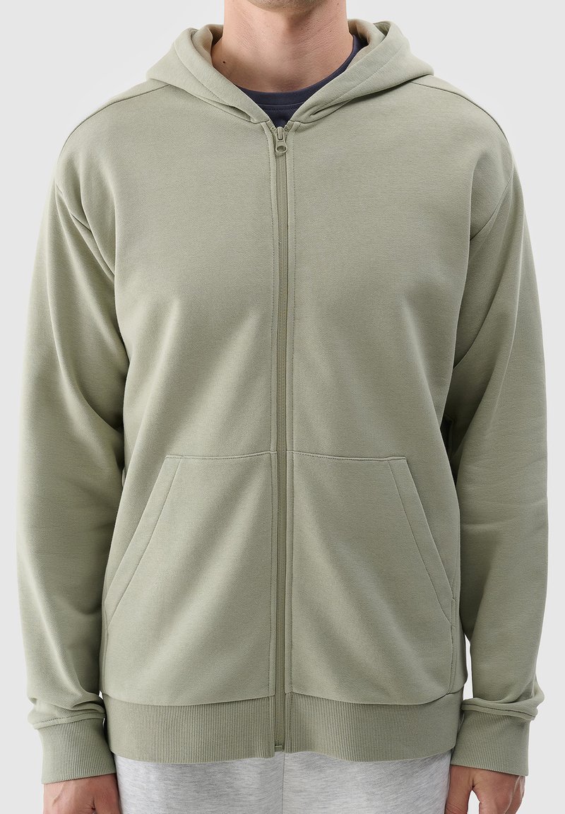 Felpa verde chiaro con zip realizzata in materiale morbido, dotata di una cerniera frontale, due tasche laterali e polsini e orlo a coste.