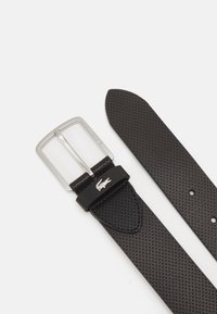 Curea din piele neagră perforată cu o cataramă rectangulară argintie și un accent cu logo. Dispune de o textură netedă și multiple găuri de ajustare.
