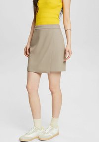 Gonna beige con un design pulito e sartoriale. Indossata con un top a coste giallo brillante e sneakers bianche con accenti gialli.
