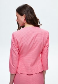 Blazer rosa a quadri con maniche a tre quarti e taglio dritto. La texture è liscia e il motivo presenta un design a griglia.