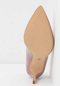 Chaussure à talon haut mauve à bout pointu avec semelle beige lisse et petit talon, positionnée à la verticale contre une surface blanche.