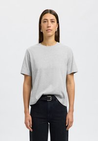 Camisa de algodón gris con cuello redondo y mangas cortas, combinada con jeans negros y un cinturón negro con una hebilla plateada.