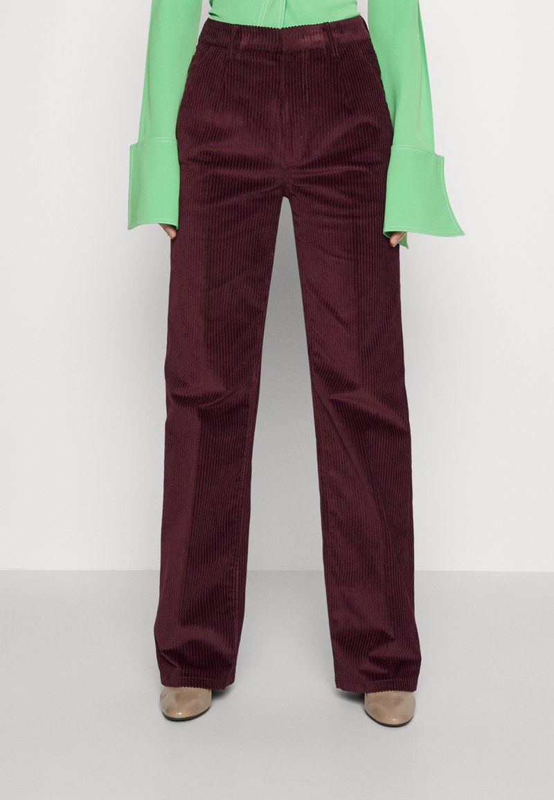 Pantalon en velours côtelé bordeaux à jambes droites porté avec des chaussures beige et un haut à manches longues vert citron avec des poignets évasés.
