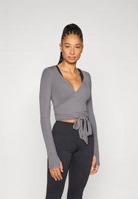 Γκρι τοπ τύπου wrap με μακριά μανίκια από ριμπ ύφασμα, με βαθύ V-λαιμόκοψη και λεπτομέρεια φιόγκου μπροστά, συνδυασμένο με μαύρο κολάν ψηλόμεσο.