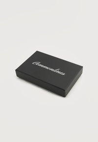 Μαύρο ορθογώνιο κουτί με την λευκή καλλιγραφική επιγραφή "Commonlines" στην κορυφή, τοποθετημένο σε απλό ανοιχτό γκρι φόντο.