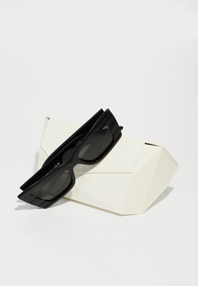Black rectangular sunglasses with curved edges and dark lenses rest on a folded white geometric case, featuring subtle branding.