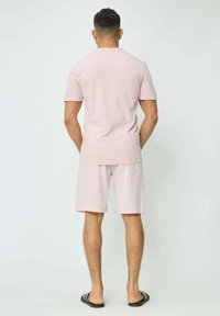 Ensemble en coton rose clair composé d'un T-shirt et d'un short à coupe décontractée, avec des manches courtes, un design uni, porté avec des sandales noires.