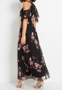 Svart maxiklänning med blommönster och axelbandslösa volangärmar, med ett rosmönster i nyanser av rosa. Avslutad med en genomskinlig, flödande textur.