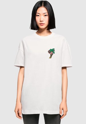 Weißes, oversized Baumwoll-T-Shirt mit einem kleinen, mehrfarbigen Grafikmotiv eines Palmenbaums und Flamingos auf der linken Brust. Kurze Ärmel, Rundhalsausschnitt.