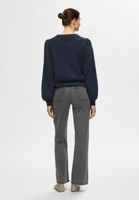 Maglione a maglia blu navy con maniche a sbuffo, abbinato a jeans grigi a vita alta e a zampa. L'outfit ha una vestibilità casual e una consistenza morbida.