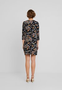 Robe noire avec un motif paisley en orange, bleu et blanc. Elle présente des manches trois quarts et une silhouette ajustée.
