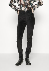 Svarta kordflöjtsbyxor med slim fit, hög midja och subtil textur. Kombineras med en blus med blommönster och svarta ankelstövlar.