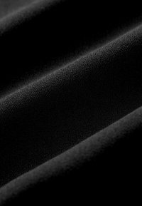 Schwarzer Stoff mit glatter Textur und subtilen Variationen, der eine gleichmäßige Oberfläche und sanfte Falten zeigt, die Tiefe erzeugen.