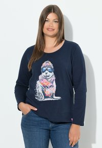 Navyblaues Langarm-T-Shirt aus weichem Stoff, mit einem bunten Hundemotiv, der eine Sonnenbrille und einen Hut trägt. Lockerer Schnitt, runder Ausschnitt.