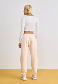 Top blanco de manga larga cortado combinado con pantalones de chándal rosa suave. El conjunto tiene un corte relajado y puños elásticos, complementado con zapatillas deportivas.