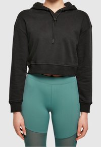 Svart beskuren hoodie med dragsko på huvan och ribbade ärmslut, kombinerad med teal leggings som har färgblockering och en mjuk yta.