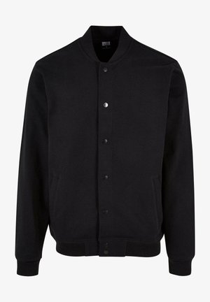 Must seest bomber-jakk, mis on valmistatud pehmest kangast, krae vaba disainiga, nupuluku ja kahe küljetaskuga. Omab ribakudumisega mansette ja alläärt.