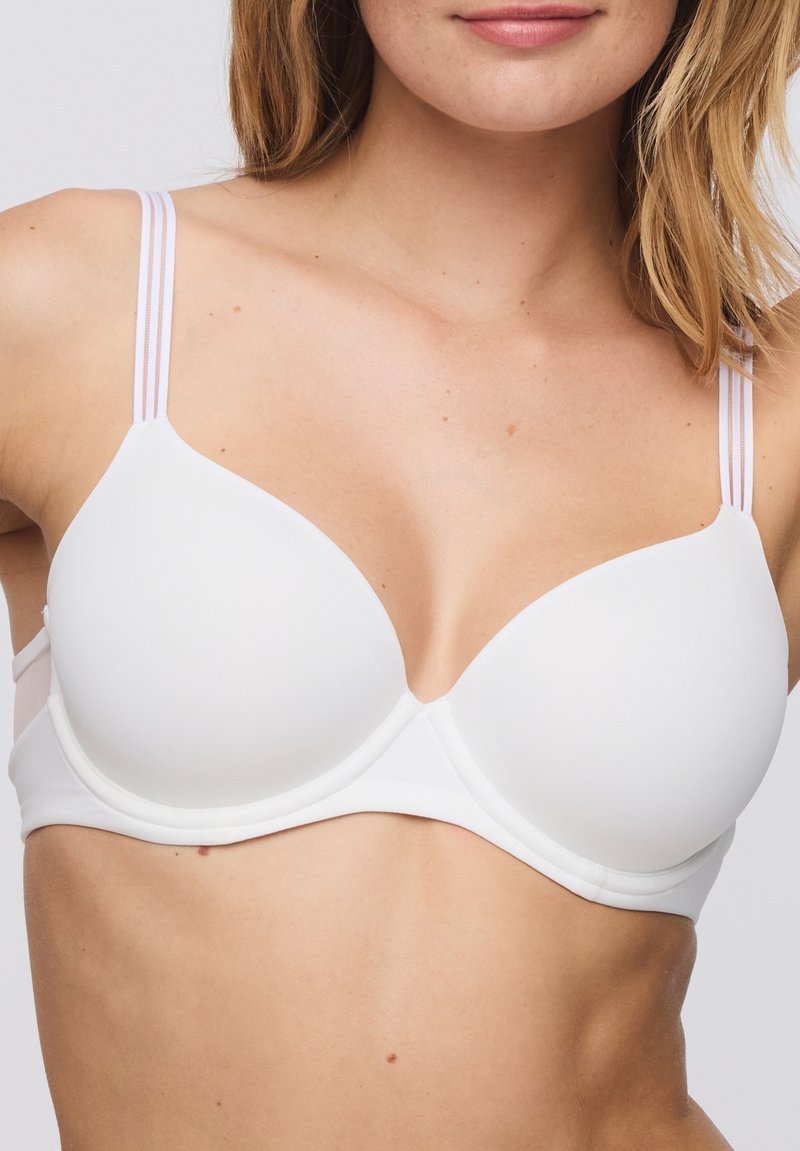 Valkoinen, pehmustettu rintaliivi, jossa on sileät kupit, kaksinkertaiset ohuet olkaimet ja saumaton muotoilu. Säädettävät hakaset takana mukautettavuutta varten.