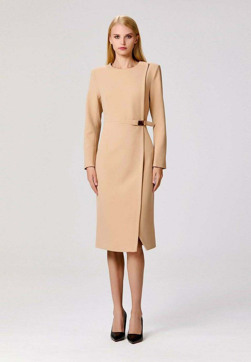 Robe beige midi à manches longues, avec un design croisé, une fente sur le côté et une ceinture étroite. Texture lisse, style minimaliste.