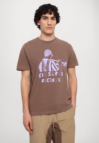 Brun bomulds t-shirt med et lilla graphic af en musiker med en trompet og teksten "KIDSUPER RECORDS." Korte ærmer og afslappet pasform.